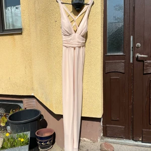 Rosa långklänning med omlott och korsade axelband - Säljer en elegant rosa balklänning med omlott framtill och v-ringning. Klänningen har breda korsade axelband i ryggen och markerad midja med draperad effekt. 