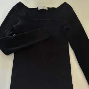 Svart ribbad långärmad topp - Säljer en svart ribbad långärmad topp med fyrkantig ringning. Materialet är stretchigt och bekvämt. Använd fåtal gånger, jättefint skick!