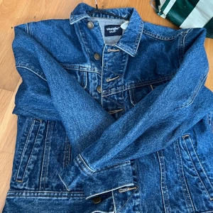 Blå jeansjacka från Wrangler Sport - Klassisk blå jeansjacka från Wrangler Sport med knappar framtill och två bröstfickor. Snygga kontrastsömmar och tidlös design som passar till det mesta. Perfekt för dig som gillar en avslappnad och cool stil.