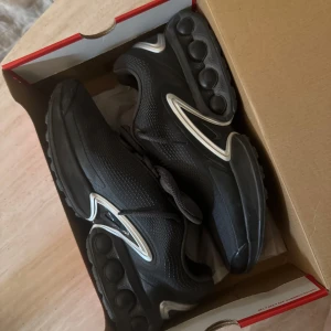 Nike air max DN - Säljer ett par svarta Nike Air Max sneakers med rund tå och platt sula. Skorna har en sportig design med synliga luftbubblor i sulan och diskreta vita detaljer längs sidorna. Perfekta för dig som gillar stilrena och bekväma sneakers.