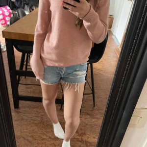 Ljusblå jeansshorts med fransar - Säljer ett par ljusblå jeansshorts med slitna detaljer och fransar nertill. Klassisk femficksmodell med råa kanter och låg midja. Perfekta för sommaren och ger en avslappnad look.