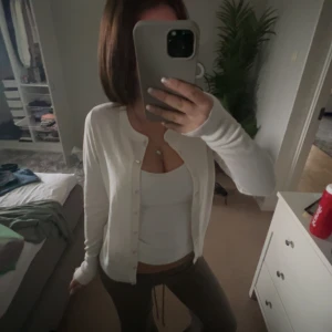 Vit kofta med knappar - Säljer en klassisk vit kofta med knäppning framtill. Koftan har lång ärm och är i ett mjukt material som passar perfekt till vardags. Enkel och stilren design som är lätt att matcha med olika outfits.