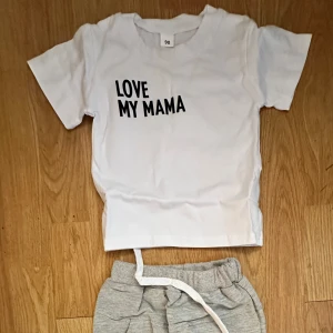 Vit t-shirt med text 'LOVE MY MAMA' - Vit t-shirt med svart tryck 'LOVE MY MAMA' på bröstet. Klassisk rund hals och korta ärmar. Perfekt för en avslappnad och lekfull stil.