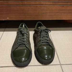 Mörkgröna sneakers från Lanvin - Säljer ett par mörkgröna sneakers från Lanvin med ovandel i mocka och tåparti i blankt material. Skorna har snörning och svarta sulor. Perfekta för dig som vill ha en stilren och unik look.