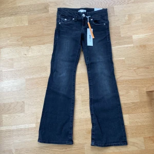 Chunky low flare jeans från Gina Tricot - Säljer ett par grå jeans från Gina Tricot med klassisk femficksdesign och silverfärgade knappar. Byxorna har en lätt utsvängd passform nertill och är tillverkade i denim med snygg tvättad look.