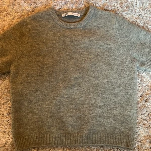 Grå stickad tröja från Zara - Mysig grå stickad tröja från Zara med korta ärmar och rund halsringning. Tröjan har ribbade muddar vid ärmslut och nederkant, perfekt för lager-på-lager-stil. (Aldrig använd, bara prövat)