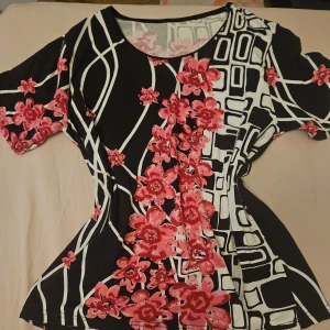 Svart och vit topp med rosa blommor - Säljer en snygg topp med svart och vit grafiskt mönster och rosa blommor. Toppen har rund halsringning och korta ärmar <3