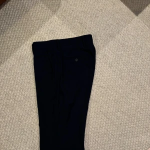 Navy kostymbyxor från Riley - Snygga Navy kostymbyxor från Riley med klassisk passform. Byxorna har diskreta fickor och stilrena detaljer, perfekta till en dressad look. Materialet känns mjukt och följsamt.