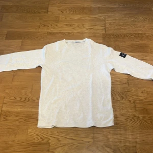 Vit långärmad tröja från Calvin Klein Jeans - Säljer en  vit långärmad tröja från Calvin Klein Jeans. Tröjan har en svart patch med CK-logga på ärmen. Tröjan är i storlek L och är nästintill aldrig använd. Hör gärna av dig vid frågor eller om det önskas fler bilder!