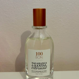 Nagaranga & Santal Citronné Eau de Parfum från 100BON - Fräsch parfym från 100BON med doft av nagaranga, sandelträ och citron. Flaskan är genomskinlig med en stilren vit etikett och har ett kopparfärgat lock. Innehåller 50 ml och är tillverkad i Frankrike med naturliga ingredienser.
