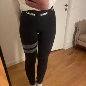 Svarta leggings från Stronger med vit detalj - Säljer dessa svarta träningsbyxor från stronger då de inte kommer till användning längre❤️Defekter förekommer, men fullt funktionella! Är även beredd att sänka priset något, så det är bara att skriva<3