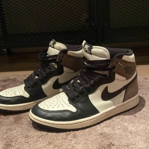 Nike Air Jordan 1 mid mocha(tar byten) - Säljer ett par Nike Air Jordan 1 High med svart, vit och brun färgkombination. Skorna har klassisk snörning, svart swoosh och hög siluett. Perfekta för dig som gillar streetwear och vill sticka ut med en ikonisk sneaker. Fint skick men man bedömer själv efter bilderna!! Ingen box eller tillbehör!