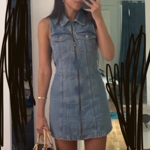 Ärmlös jeansklänning med dragkedja - Säljer en snygg ärmlös jeansklänning med dragkedja framtill och klassisk krage. Klänningen har fickor på bröstet och markerad midja för en cool och avslappnad look. Perfekt till sneakers eller boots.