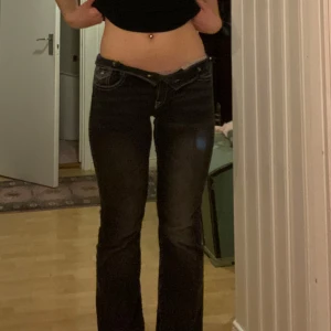 Svarta bootcut jeans med vita sömmar - Säljer ett par svarta bootcut jeans med tydliga vita sömmar och klassiska fickor bak med knappdetalj. Liknar true religion. Jeansen har låg midja och går även att vika ner om man vill ha ännu lägre och lätt utsvängda ben, perfekt för en avslappnad men snygg look. Passar mig som är 170 och brukar ha S/M