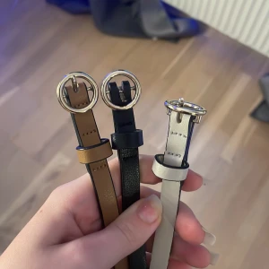 Tre smala bälten med rund spänne - Säljer tre smala bälten i olika färger: beige, svart och brun. Alla har ett runt, silvrigt spänne och är tillverkade i skinnimitation. Perfekta för att ge en snygg touch till din outfit.
