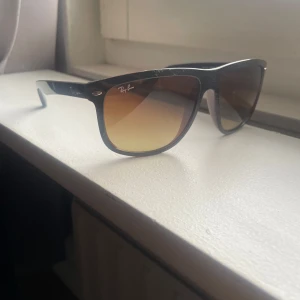 Svarta solglasögon från Ray-Ban - Klassiska svarta solglasögon från Ray-Ban med bruntonade glas och Wayfarer-inspirerad form. Snygg metallogo på skalmen och diskret Ray-Ban-logga på linsen. Perfekt accessoar för soliga dagar. Priset är inte hugget i sten kan gå ner i pris vid snabb affär.