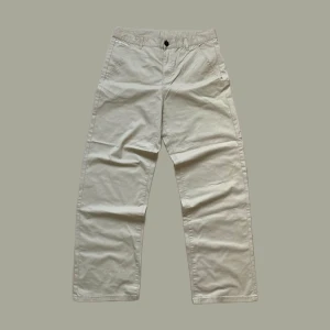 Beige chinos från Woxor Urban Streetwear - Snygga beige chinos från Woxor Urban Streetwear med raka ben och klassisk passform. Byxorna har framfickor, bakfickor och stängs med knapp och dragkedja. Perfekta för en clean och stilren look.