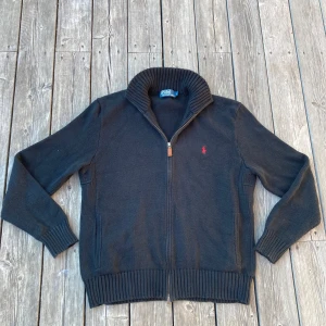Svart stickad kofta från Polo Ralph Lauren - Svart Ralph Lauren tröja/zip up i storlek L som passar sin storlek bra. Tröjan är i mycket bra skick utan några defekter samt har ett dubbel dragkedjesystem. Färgen är svartare än den ser ut på bilden. Hör av er om frågor!
