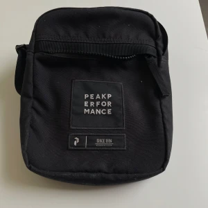 Svart axelväska från Peak Performance - Säljer en svart axelväska från Peak Performance med justerbar rem och dragkedja. Väskan har en enkel, stilren design med logotyp framtill och en praktisk ytterficka.Har använts få gånger.Ny pris är 450kr