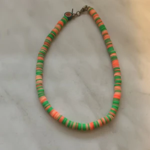 Färgglatt pärlhalsband i orange och grönt - Säljer ett halsband med platta pärlor i orange och grönt. Halsbandet har ett enkelt lås i metall och är perfekt för att ge en färgklick till din outfit.