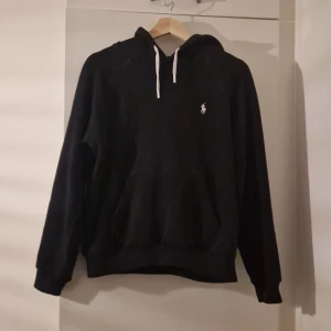 Svart ralph lauren hoodie  - Säljer en stilren svart hoodie från Polo Ralph Lauren med vit dragsko och det klassiska logotypen på bröstet. Perfekt för en avslappnad look.  Nypris 2000+! Mitt pris endast 599🤩🚀 Priset går att diskutera vidare snabb affär!
