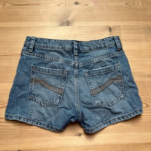 lågmidjade jeansshorts - Klassiska blå jeansshorts med två bakfickor och bälteshällor. Shortsen har knapp och dragkedja framtill samt synliga sömmar i kontrastfärg. Perfekta för varma dagar och enkel att matcha med olika toppar.