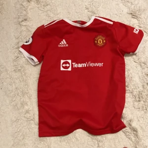 Manchester United Ronaldo  - Röd Manchester United fotbollströja med vita detaljer, Adidas-logga och TeamViewer sponsortryck. Nummer 7 och Ronaldo på ryggen, Premier League-märke på ärmen och Kohler-tryck. Klassisk design med rund hals och korta ärmar och är från 2022. Priset kan alltid diskuteras 