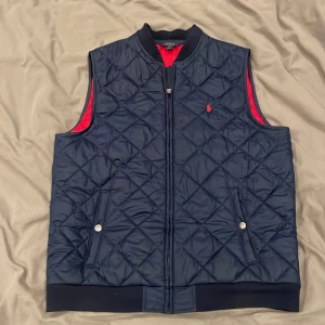 Mörkblå quiltad väst från Polo Ralph Lauren - Säljer en mörkblå quiltad väst från Polo Ralph Lauren med dragkedja framtill. Västen är som ny och är i storleken XL för barn men fungerar perfekt som S. 