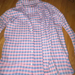 Rutig skjorta från Tommy Hilfiger - Säljer en snygg rutig skjorta från Tommy Hilfiger i rosa och blått. Skjortan har långa ärmar, klassisk krage och knäppning framtill. Perfekt för dig som gillar färg och mönster!