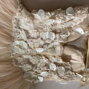 Specialdesignad bröllopsklänning  - (Klänning är specialdesignad )Drömmig midiklänning  i champagnefärgad tyll med 3D-blommor och blad på livet. Klänningen har axelbandslös design och vackra spetsdetaljer, perfekt för speciella tillfällen. Kjolen är voluminös och ger en sagolik känsla. 