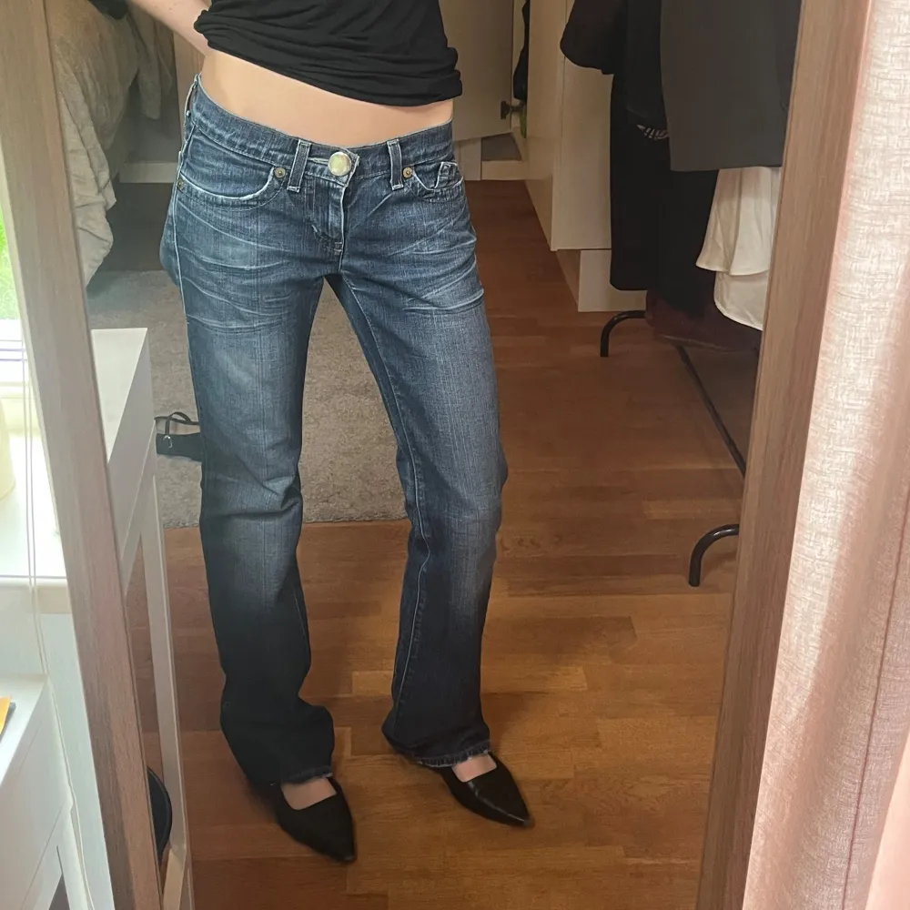 Säljer ett par blå jeans med bootcut passform och snygga broderade detaljer på bakfickorna. Jeansen har låg midja, klassisk femficksdesign och är tillverkade i denim med ljusa slitningar. Perfekta för en avslappnad och trendig look. Midjemått: 38 cm innerbenslängd: 82 cm. Farkut & Housut.