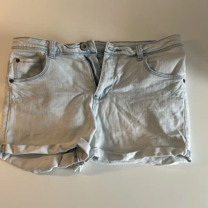 Ljusblå jeansshorts - Säljer ett par ljusblå jeansshorts med klassisk femficksdesign och uppvikta benslut. Shortsen har bälteshällor och knappgylf. Perfekta för varma dagar och enkel att matcha med olika toppar. Säljer för att de var för små när jag fick dem men kunde ej returnera.