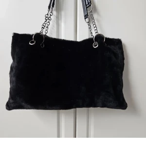 Svart fluffig axelväska - Säljer en svart axelväska med mjuk, pälsliknande yta och silverfärgade kedjeremmar. Får plats med mycket saker i, oanvänd