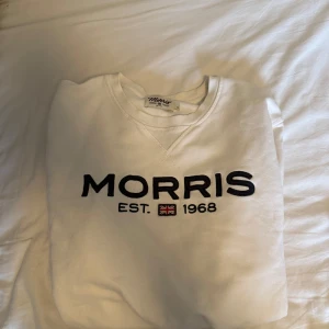Vit sweatshirt från Morris - Vit sweatshirt från Morris med svart broderad logga och texten 'EST. 1968' framtill. Klassisk rund halsringning och mjukt material, perfekt för en stilren och avslappnad look. Som ny och inga flaws. Nypris runt 1000