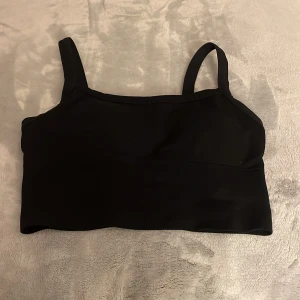 Svart croppad linnetopp - Säljer en enkel och stilren svart croppad linnetopp med smala axelband. Perfekt att ha på sig när man tränar. Toppen är ärmlös och har en rak passform.