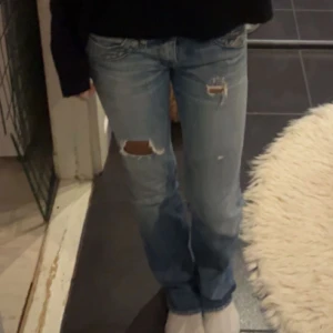 Ljusblå slitna jeans - Säljer ett par ljusblå jeans med slitningar på låret och knät. Jeansen har klassisk femficksdesign och normal passform. Perfekta för en avslappnad och trendig look.