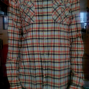Rutig somrig skjorta med långa ärmar - Säljer en långärmad rutig skjorta, med bröstfickor och knappar framtill. Skjortan har en mix av färger som orange, gul, vit och brunt. Perfekt för dig som gillar en avslappnad och klassisk stil. Från  lack Temple storlek L, large