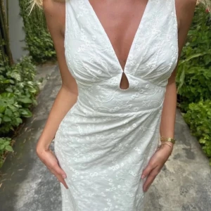 Helt slutsåld adoore klänning - Supersnygg vit långklänning med djup v-ringning och liten cut-out framtill. Klänningen har broderade blommor i tyget och är ärmlös med figurnära passform. Perfekt för sommarens alla tillfällen!  Student mottagning klänning  