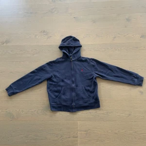 Marinblå hoodie från Polo Ralph Lauren - Trendig Polo Ralph Lauren sipper, bra skick, storlek 14-16/L, normal i storleken. OBS! Liten fläck på en av ärmarna. Ny pris 1200kr