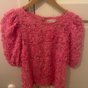 Rosa blommig blus Holly & Whyte - Superfin rosa blus från Holly & Whyte med blommor och spetsdetaljer med puffiga korta ärmar. 