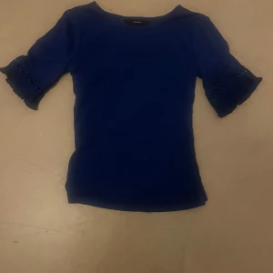 Blå topp med spetsärm från Vero Moda - Supersnygg marinblå topp från Vero Moda i storlek XS. Toppen har korta ärmar med fina spetsdetaljer och broderade cirklar som ger en unik look. Perfekt för dig som vill ha något enkelt men ändå med en twist.