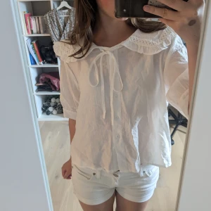 Vit blus med krage och knyt - Supersöt vit blus med volangkrage och knytband framtill. Blusen har knappar hela vägen och korta ärmar. Perfekt för dig som gillar romantisk och trendig stil. Materialet känns lätt och luftigt, perfekt för varmare dagar. Har köpt den i Korea