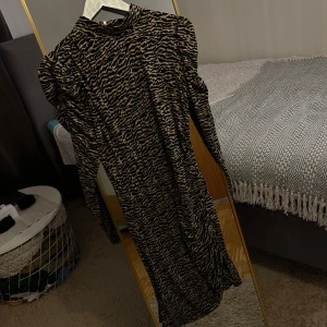 Zebramönstrad långklänning Vero Moda - Cool långklänning från Vero Moda med zebramönster i svart och beige. Klänningen har puffade axlar, lång ärm och hög hals. Materialet är mjukt och stretchigt, perfekt för dig som vill sticka ut med en edgy look.