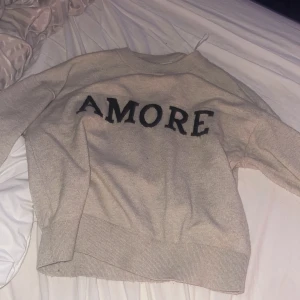 Beige stickad tröja med svart text Gina Tricot - Beige stickad tröja från Gina Tricot med svart texten 'AMORE' framtill. Tröjan har rund halsringning, ribbade muddar och lång ärm. Perfekt för dig som gillar en enkel men ändå statement look. Storlek xs,s  slutsåld 