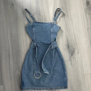 Jeansklänning med bälte från H&M Divided - Snygg jeansklänning i blå denim från H&M Divided. Klänningen är för barn och har smala axelband, markerad midja med tillhörande bälte med metallring och dragkedja bak. Perfekt för dig som gillar en cool och avslappnad stil.