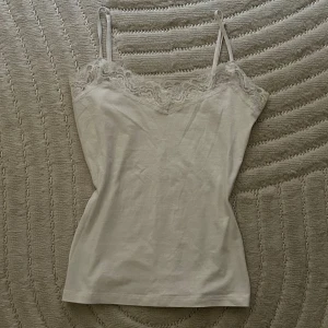 Vit linnetopp med spetskant - Säljer en söt vit linnetopp med tunna axelband och fin spetsdetalj längs urringningen. Toppen är ärmlös och har en enkel, klassisk passform som funkar till många olika stilar. M/S