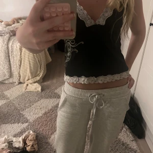 Svart linnetopp med spetsdetaljer - Supersöt svart linnetopp med tunna axelband och v-ringning. Toppen har ljus spets längs halsringningen och nederkanten samt ett dekorativt tryck på ena sidan. Perfekt för dig som gillar en feminin och trendig look. pris kan diskuteras 