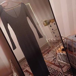 Klänning  - Snygg långklänning i mörkgrått med ribbad struktur och v-ringad hals. Klänningen har lång ärm och figurnära passform som framhäver siluetten. Perfekt för dig som gillar stilrena och enkla plagg med en modern touch.