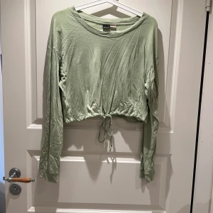 Ljusgrön croppad tröja med snörning - Snygg ljusgrön croppad tröja med långa ärmar och snörning i midjan. Perfekt för dig som gillar en avslappnad och trendig stil. Mjuk och skön bomullskänsla, passar till både jeans och kjol.