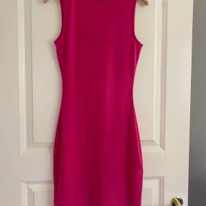 Rosa kortklänning från NA-KD XXS -  ärmlös kortklänning i stark rosa från Melissa Bentsen x NA-KD. Klänningen har en tight passform och är tillverkad i ett tunt, lätt material som är ganska genomskinligt